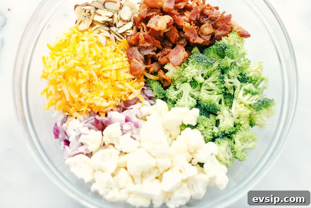 Cauliflower broccoli salad is filled with fresh florets and red onions, bacon pieces with chunks of cheese making this the perfect side salad. Shredded cheese, sliced almonds, bacon chopped up, broccoli and cauliflower florets and red onion chopped up separated in a glass bowl.