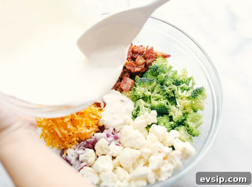 Cauliflower broccoli salad is filled with fresh florets and red onions, bacon pieces with chunks of cheese making this the perfect side salad. All the ingredients chopped up with the mayonnaise dressing being poured overtop.