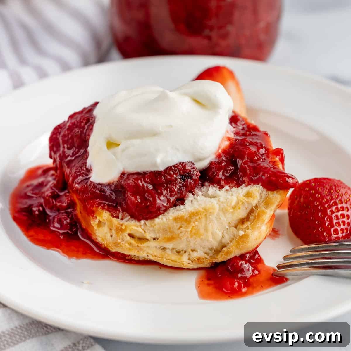 Homemade Strawberry Compote: Quick Recipe for Desserts 10 A biscuit on a white plate topped with strawberry sauce and whipped cream.