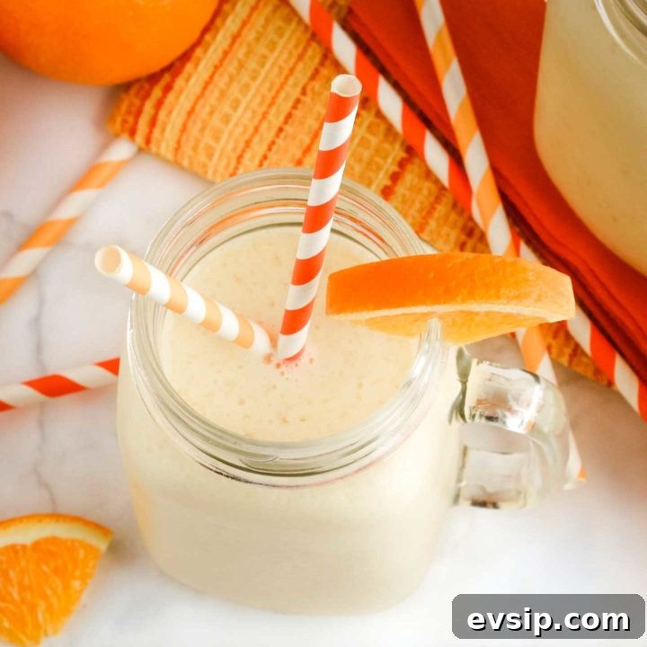 Finished smoothie in a clear glass mug with two striped orange straws and a wedge of orange on the rim.