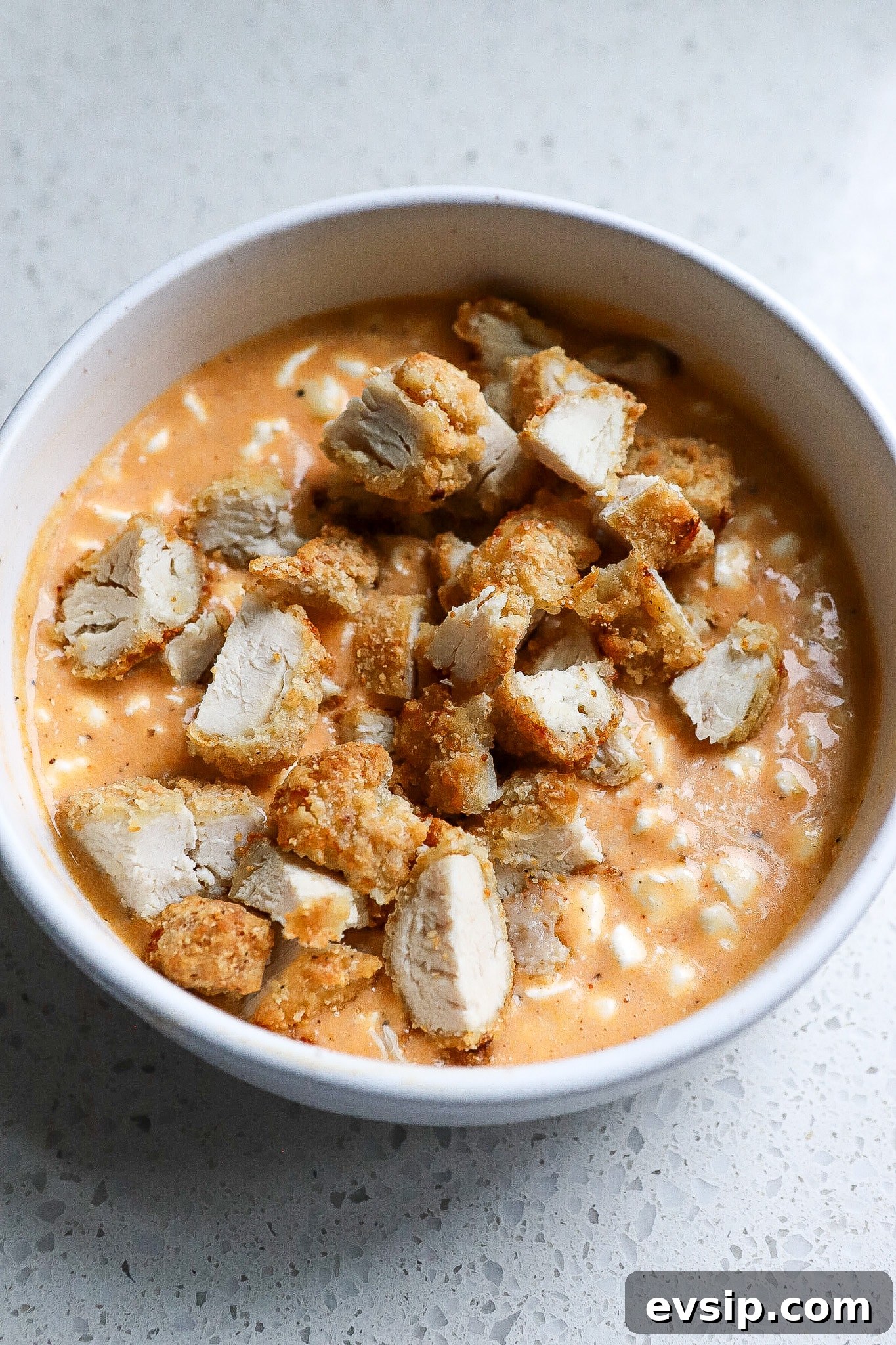 Buffalo Chicken Cottage Cheese Bowl for High-Protein Meals 3 Side angle of chicken tenders cut up in a bowl with buffalo sauce and cottage cheese.