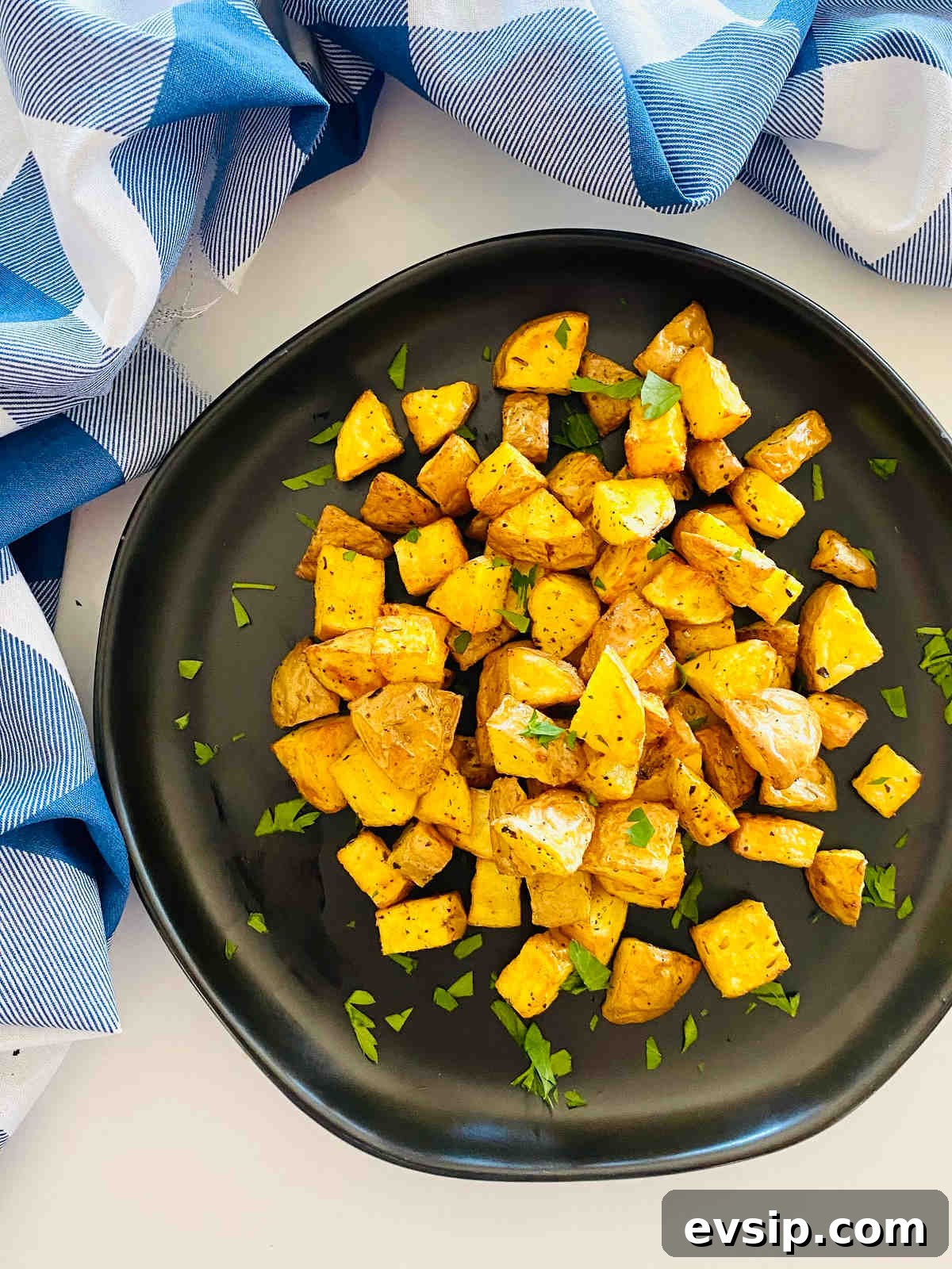 Crispy Air Fryer Diced Potatoes You’ll Love 2 diced potatoes cooked in air fryer on a plate with parsley garnish and a blue napkin