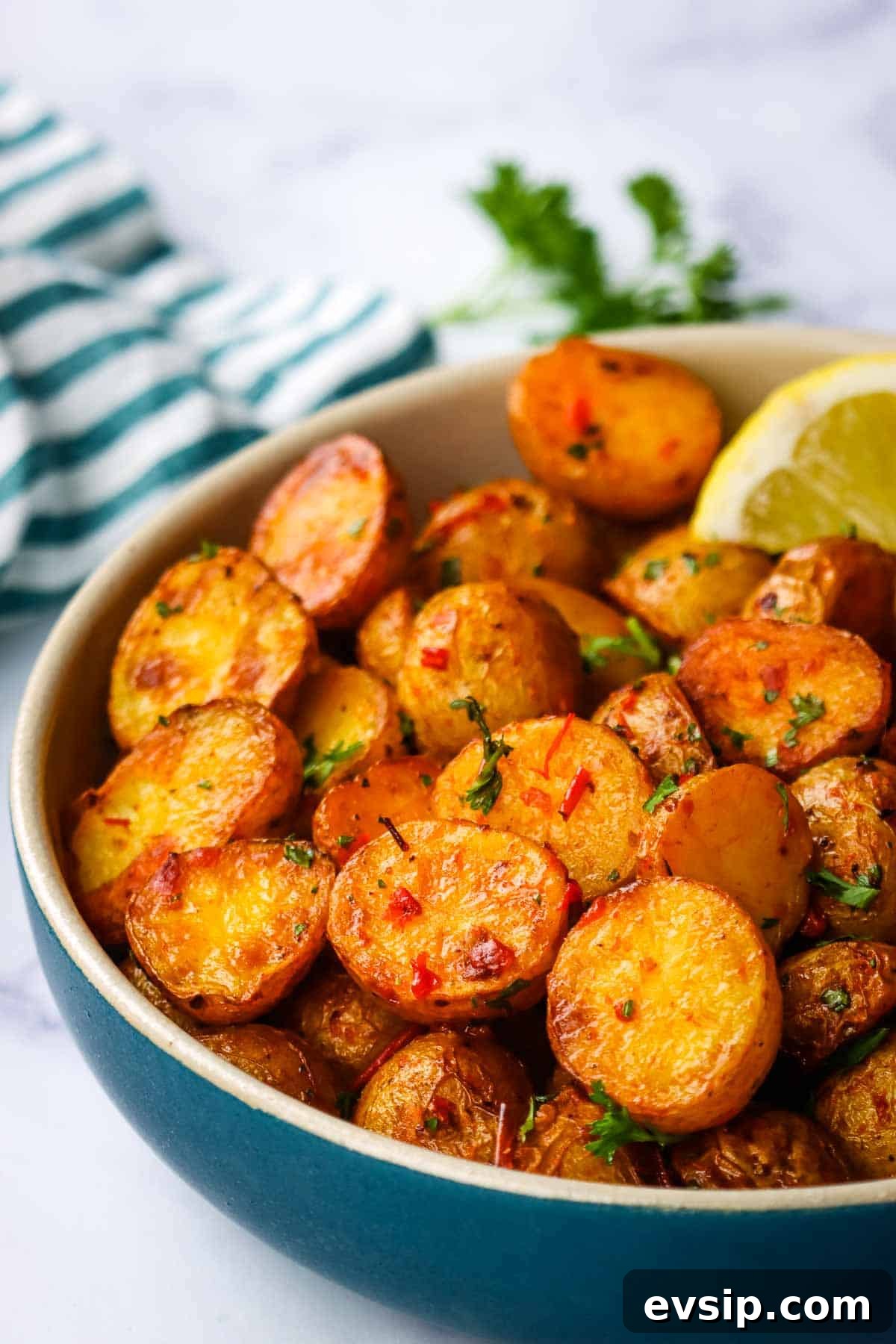 A bowl of roasted harissa potatoes garnished with parsley and a lemon wedge.