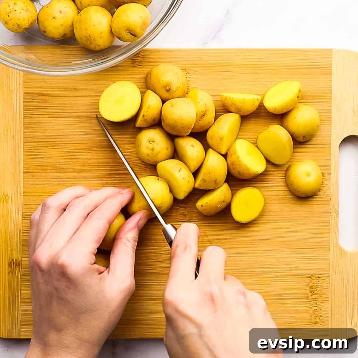 chopping baby potatoes in half on a cutting board