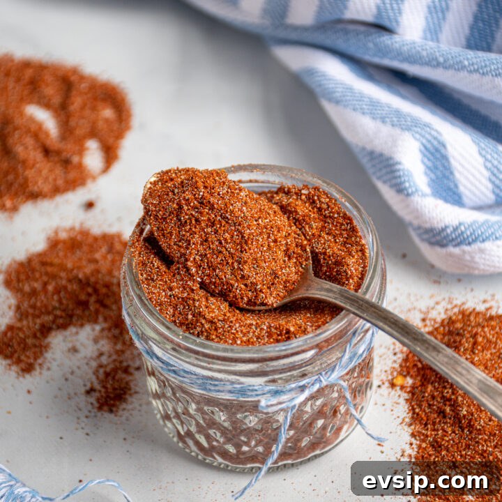 Spoon filled with fajita seasoning laying on top of a full jar of spices.