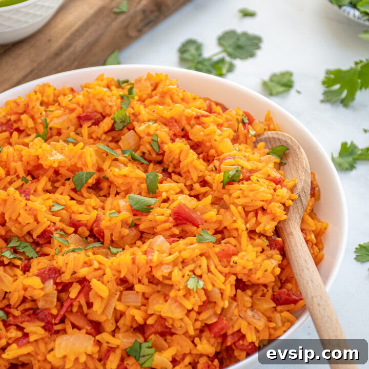 Bright orange-red colored Mexican Rice in a large white bowl with a wooden spoon garnished with chopped cilantro.