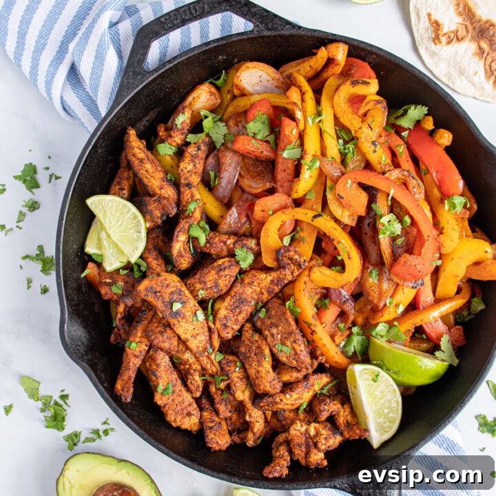 Overhead of a cat iron filled with skillet chicken fajitas and bright colored bell peppers garnished with pieces of cilantro.
