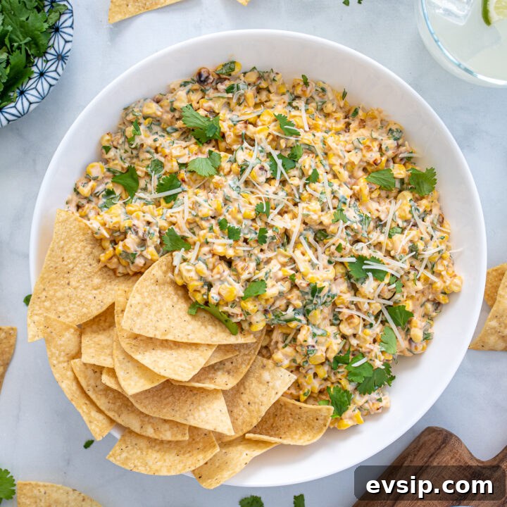 Large what bowl filled with Mexican Street Corn Dip and tortilla chips surrounded by more chips, cilantro, and limes.