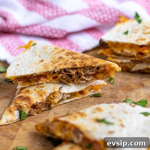 two pieces of carnitas quesadillas stacked on top of each other showing the pork and cheese on the inside