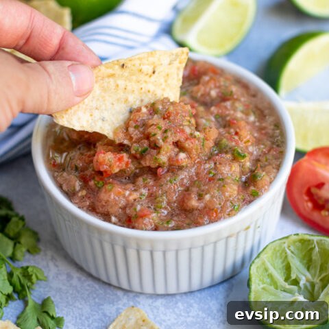fresh restaurant style salsa being scooped out of a white bowl with a tortilla chip