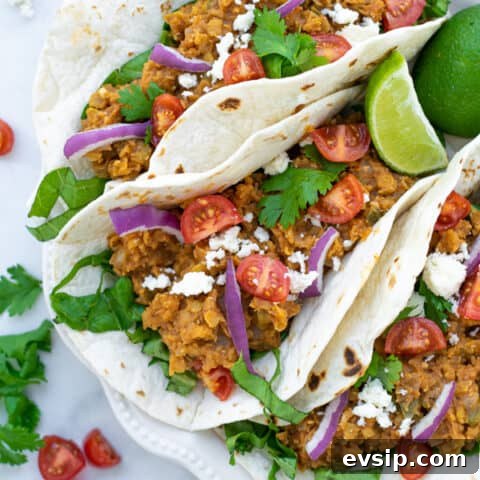 three red lentil tacos with vegetarian taco meat on a white plate with garnishes