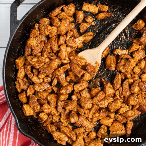 Easy Chicken Tacos being made in a cast iron pan, saucy chicken pieces covered in seasoning.