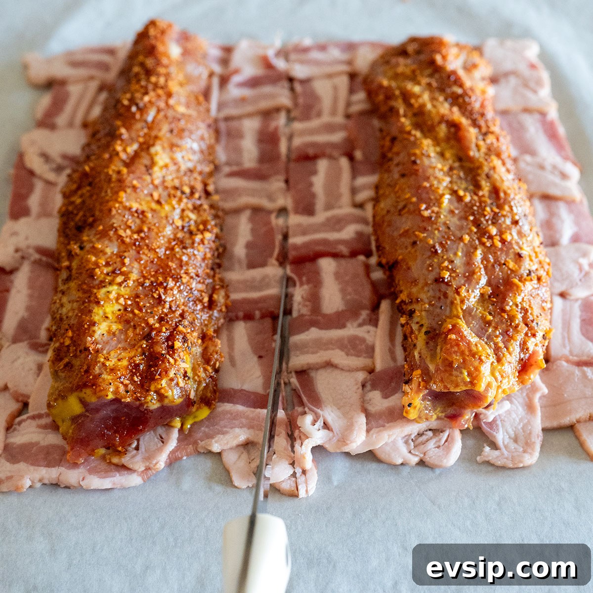 two pork tenderloins on bacon weave while knife is slicing weave in half.
