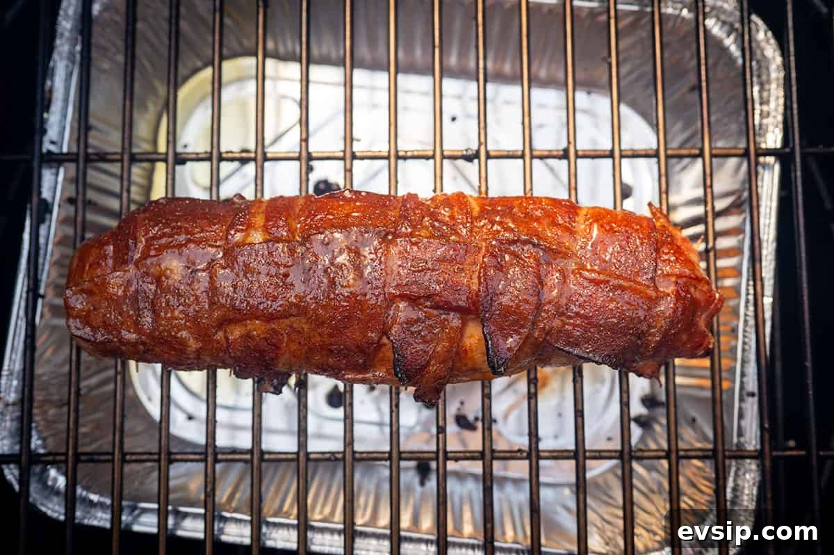 bacon-wrapped pork tenderloin getting crispy on grill.