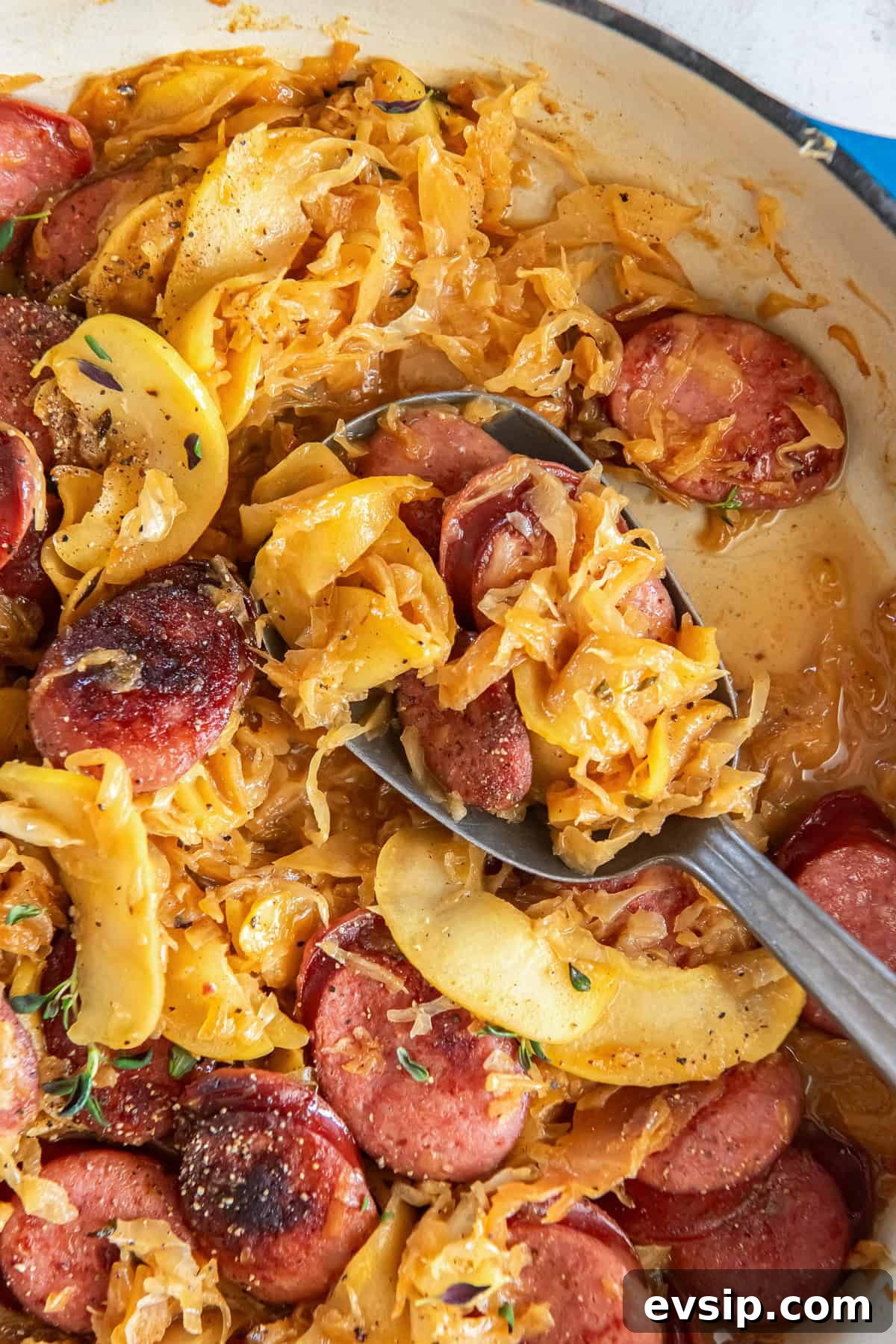 A spoon scooping kielbasa and sauerkraut from a skillet.
