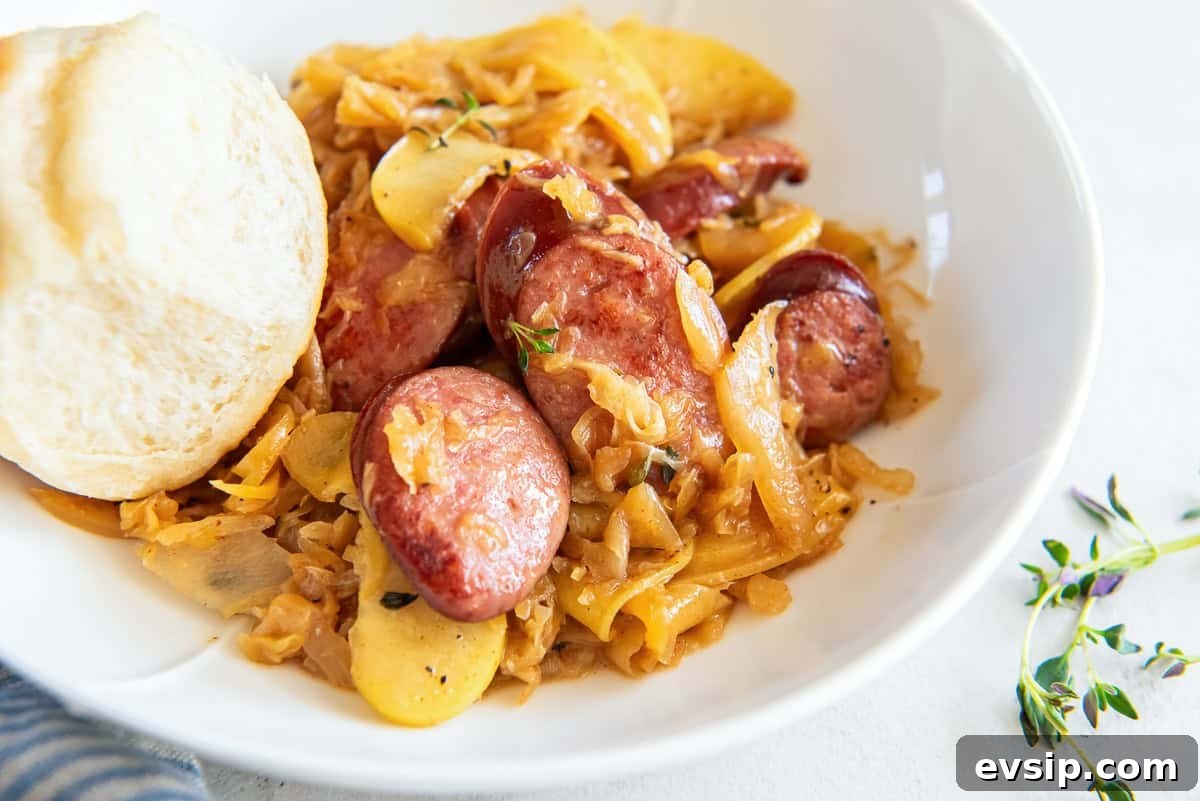 A serving of kielbasa and sauerkraut in a white bowl with a dinner roll.