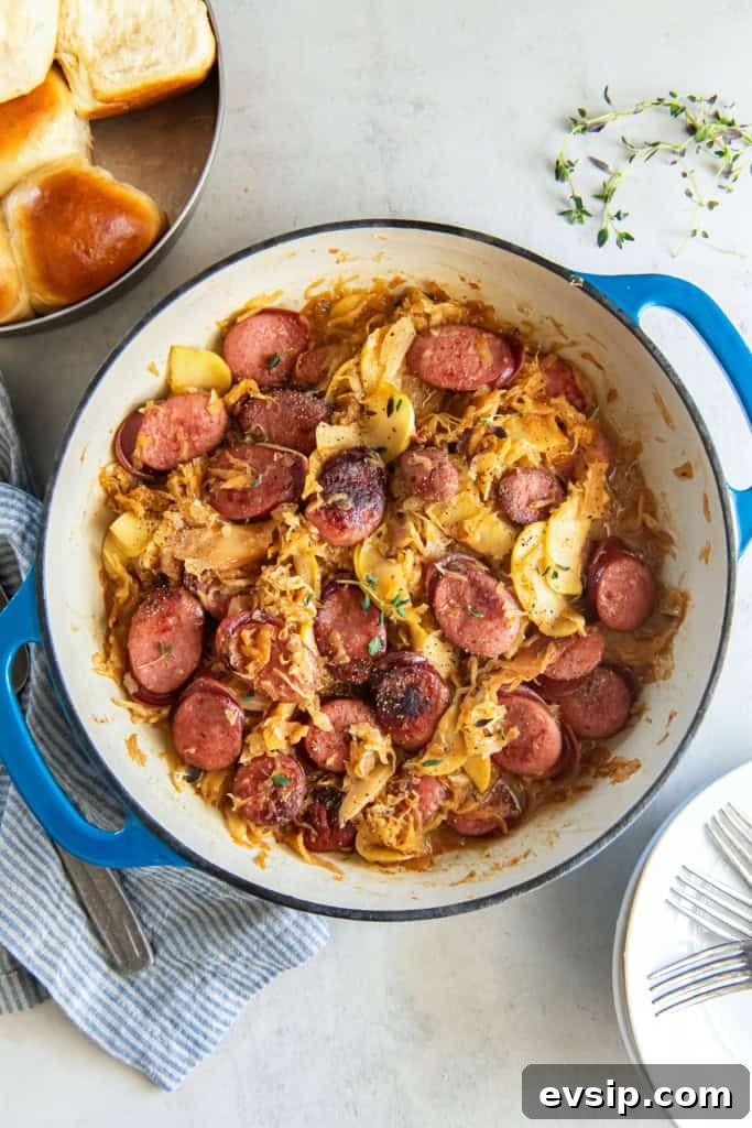Kielbasa and sauerkraut with apples in a skillet next to a pan of dinner rolls.