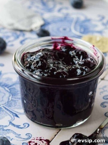 Close-up of blueberry earl grey jam on blue tile in a small glass jar.