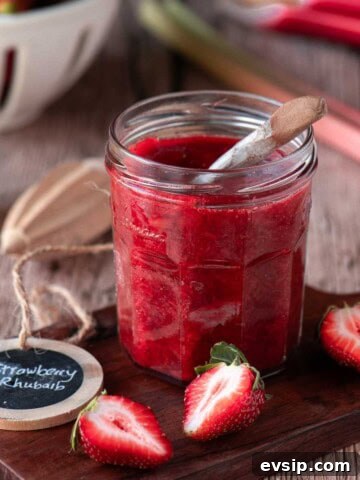 Strawberry rhubarb jam on a wood board with fruit scattered around it.