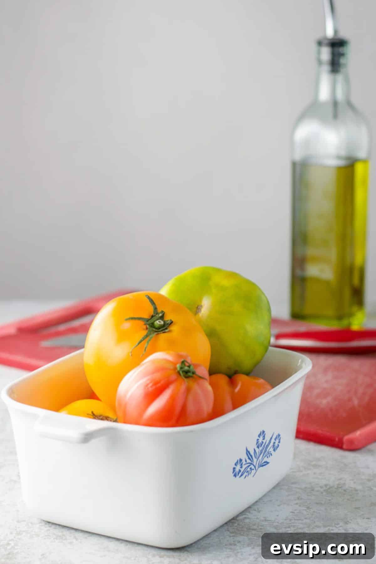 Sweet Baked Tomatoes with Honey-Glazed Juiciness 4 Tomatoes in a bowl with a red board, knife and oil in the background