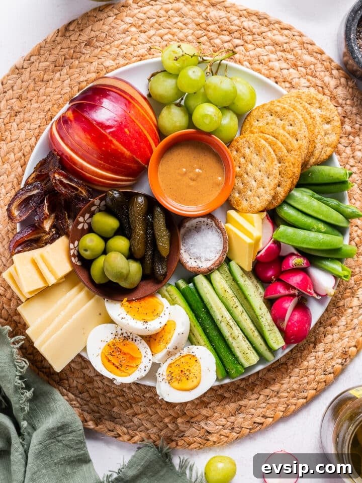 balanced snack plate with grapes, apples, dates, peanut butter, crackers, snap peas, radishes, cucumbers, cheese, eggs and olives