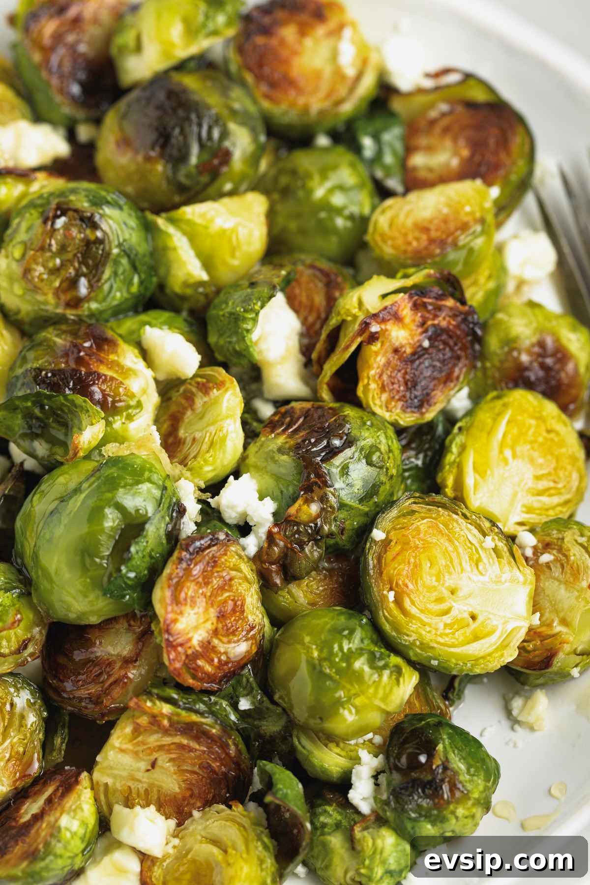 Roasted Brussels Sprouts with Goat Cheese and Honey Glaze 4 Roasted brussels sprouts with goat cheese crumbles and drizzled with honey on a round white plate.