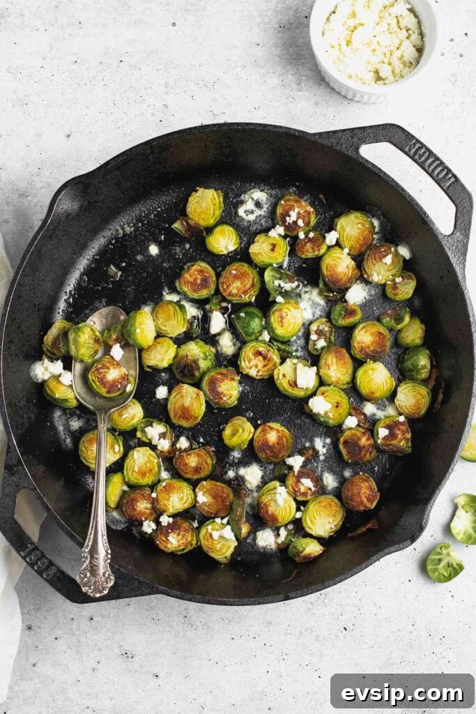 Roasted Brussels Sprouts with Goat Cheese and Honey Glaze 8 Roasted Brussels sprouts with goat cheese crumbles in a cast iron skillet with a vintage spoon.