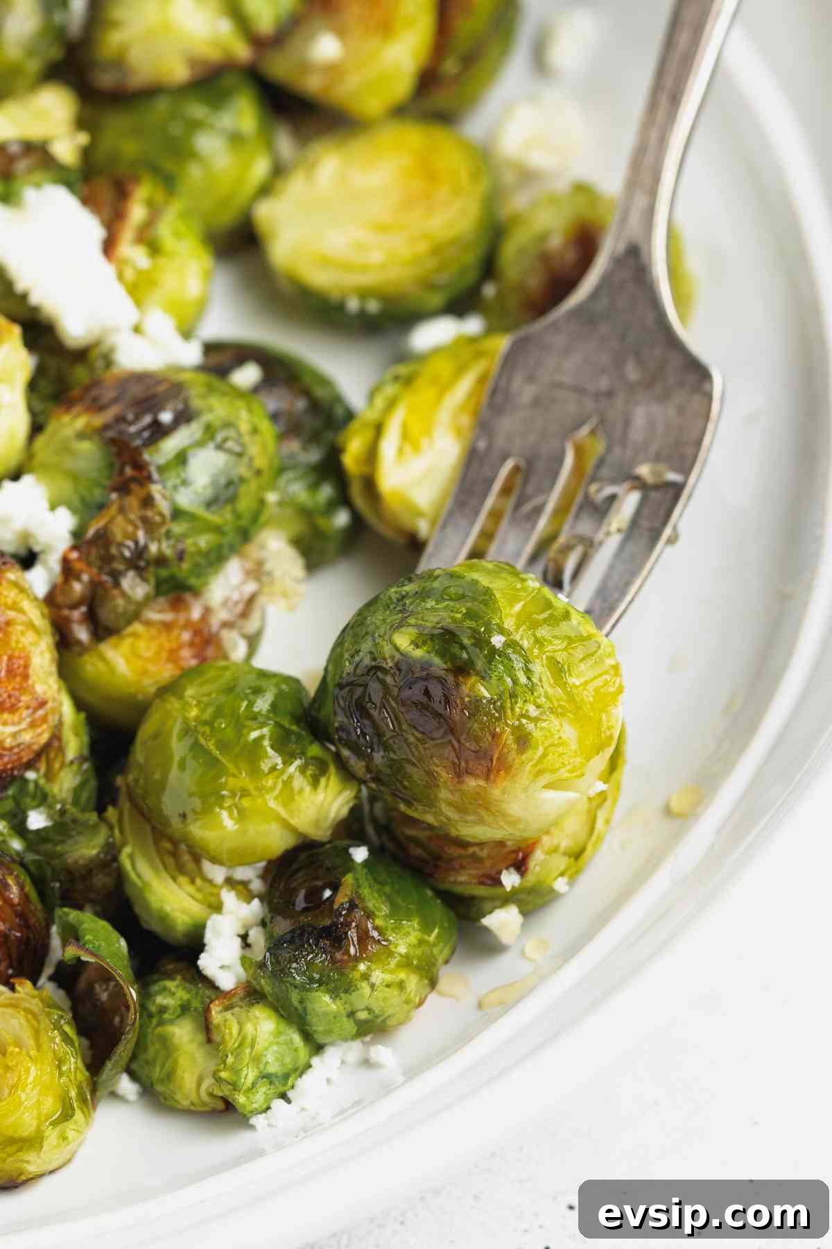 Roasted Brussels Sprouts with Goat Cheese and Honey Glaze 9 Vintage fork grabbing a crisped Brussels sprout from a round plate.