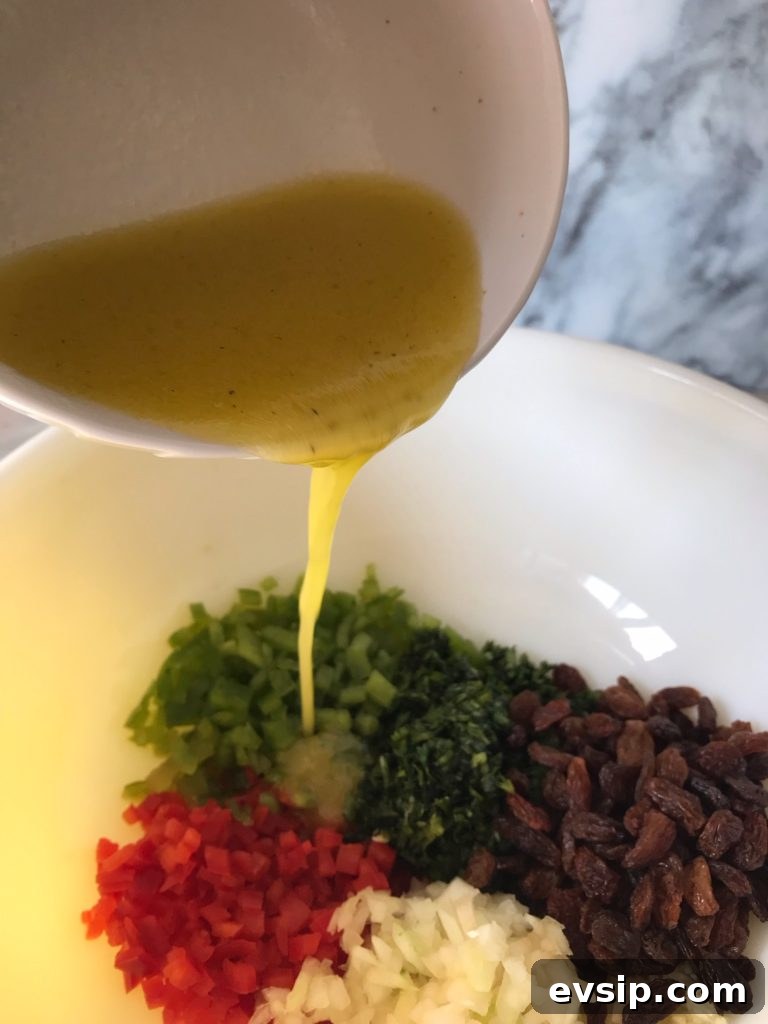 a freshly made lemon olive oil vinaigrette being poured into a bowl of chopped vegetables and raisins 