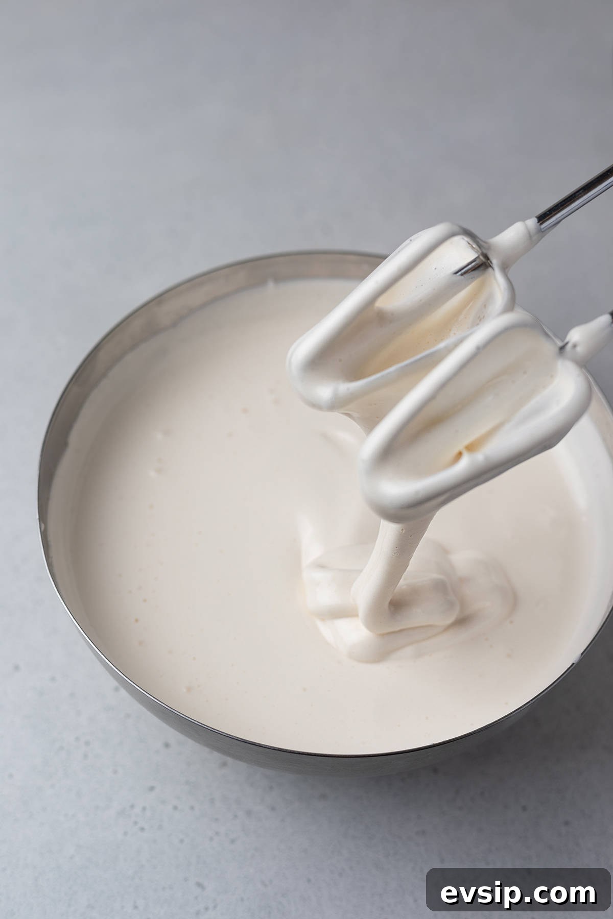 Beaten egg mixture in a bowl with a ribbon stage on mixer beaters.