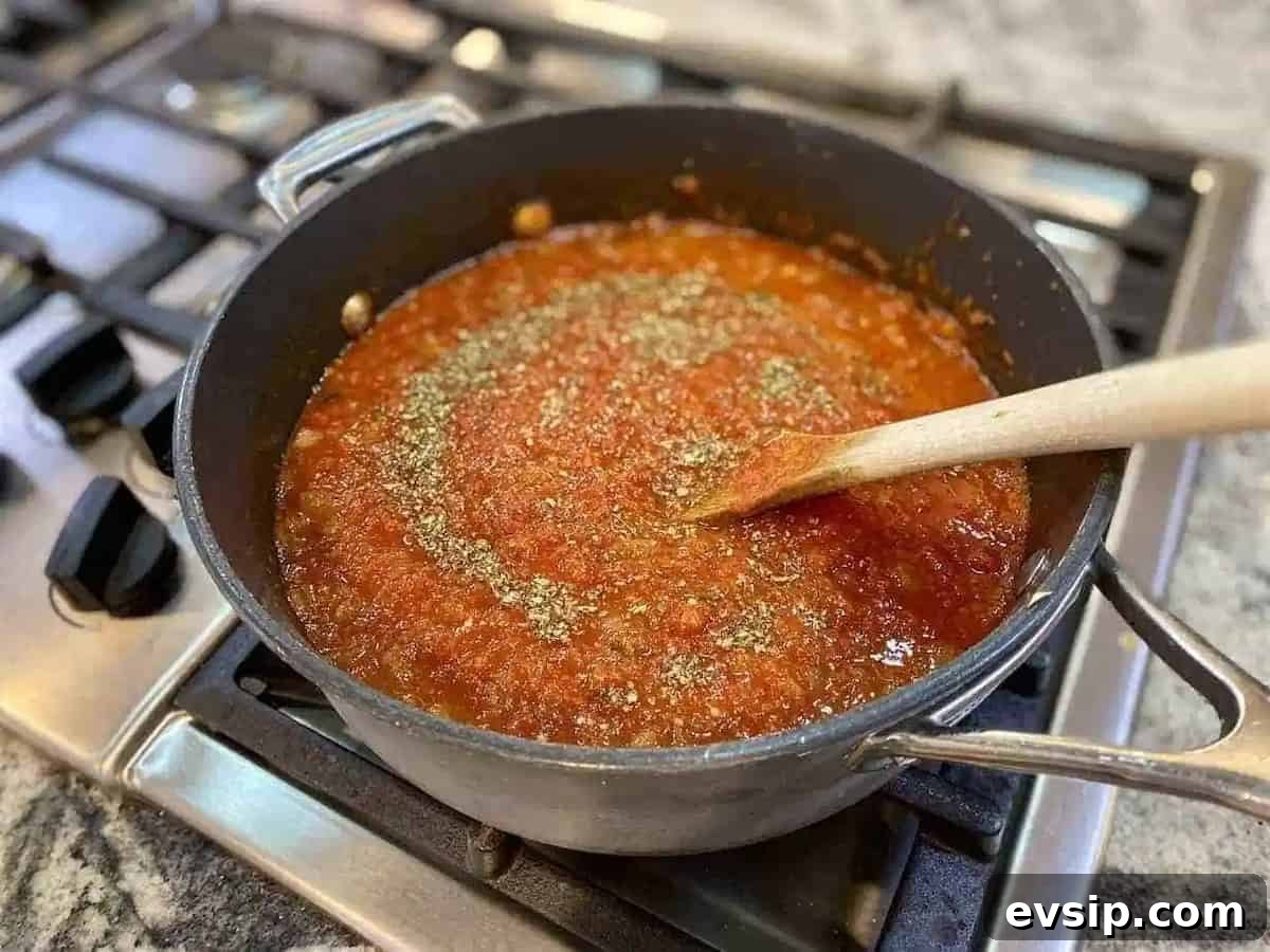 Vegan Marinara Sauce in a pot on the stove with a wooden spoon on the stove.