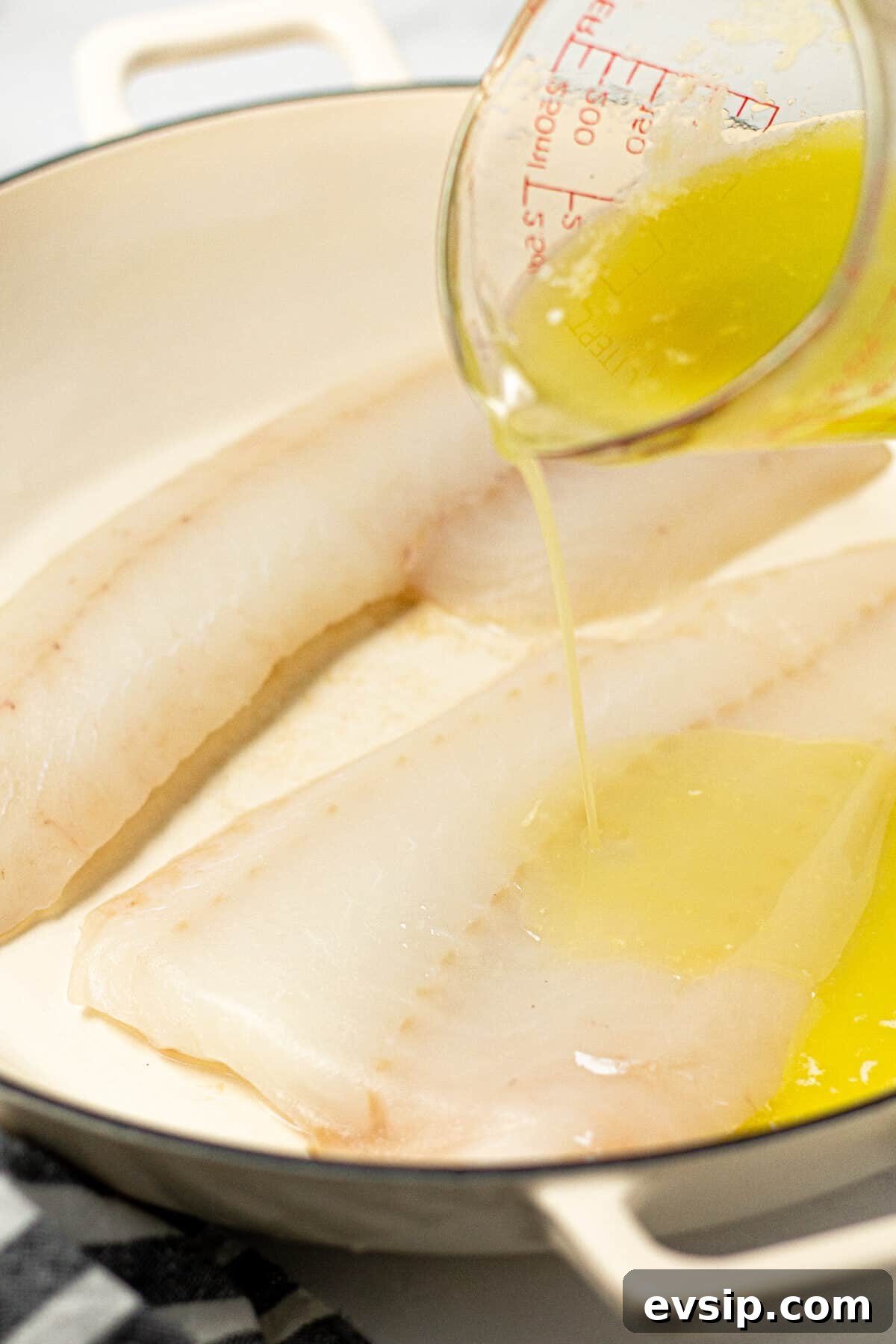 A baking dish with two fish fillets with butter being poured over them