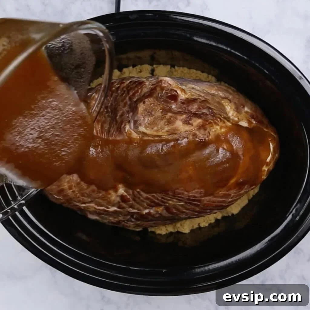 Sauce being poured on a spiral ham in a crockpot.