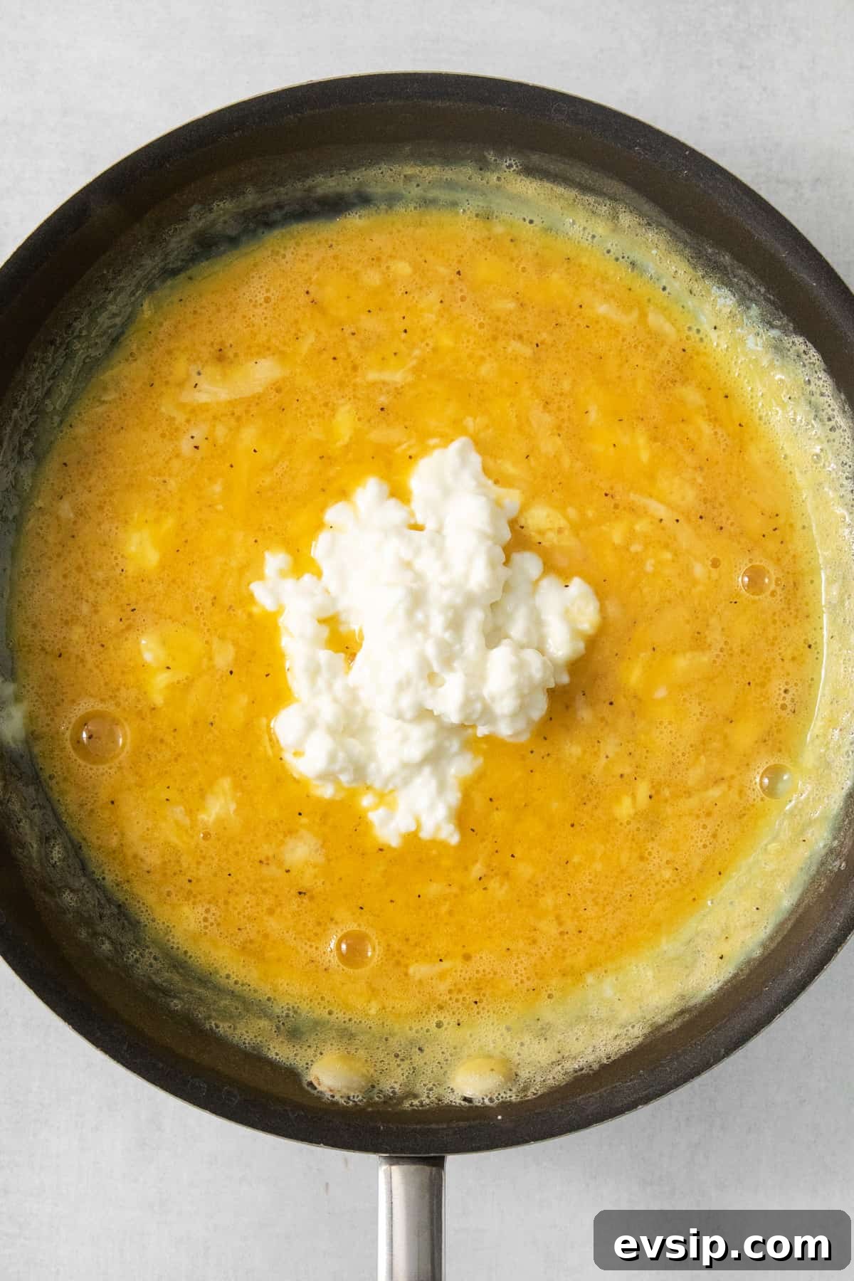 A frying pan with a yellow sauce and feta cheese.