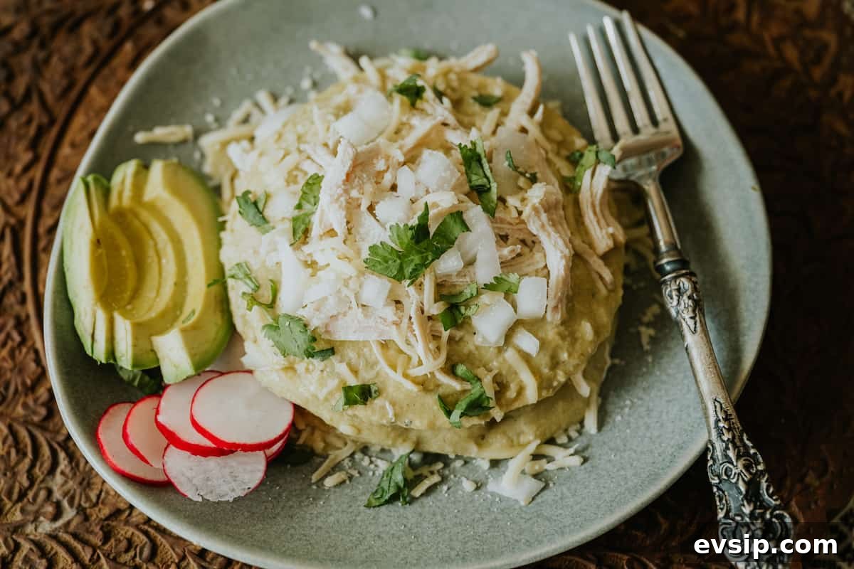 Authentic Green Enchiladas (Enchiladas Verdes) Recipe for Dinner 11 Flat lay of a pale green plate with a stacked serving of enchiladas verdes, garnished with creamy green chile sauce, and served alongside fresh avocado and radish slices.