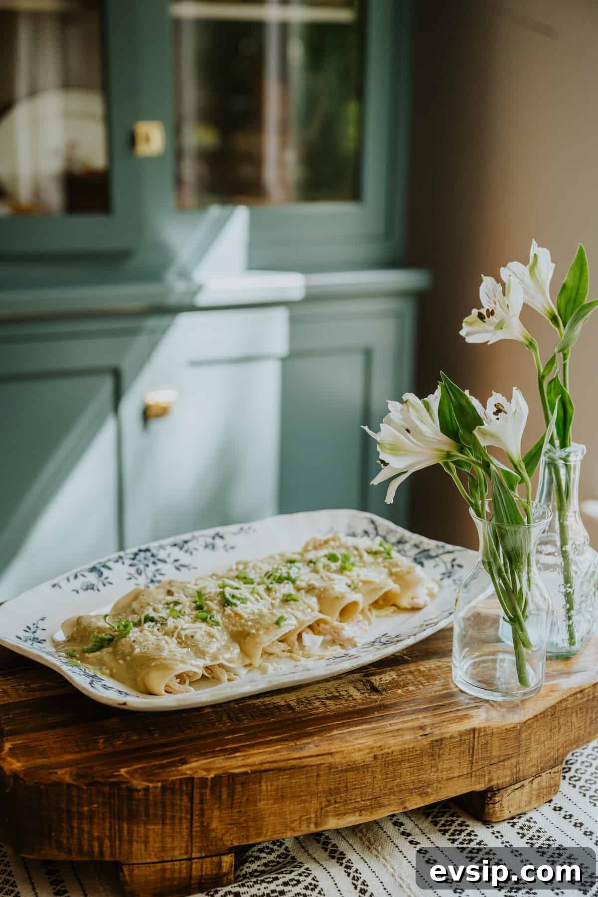 Authentic Green Enchiladas (Enchiladas Verdes) Recipe for Dinner 13 Wooden tray holding a serving platter of enchiladas verdes topped with cheese and cilantro, styled alongside two vases filled with fresh flowers for a cozy, inviting presentation.