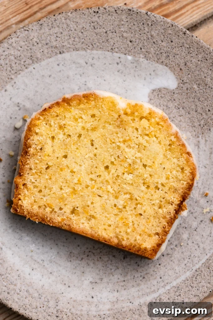 Overhead view of a slice of orange cake with vanilla icing on a plate.