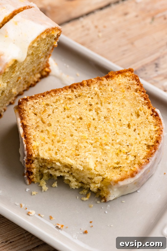 Slice of orange cake with vanilla icing on a tray with a corner cut off the cake slice.