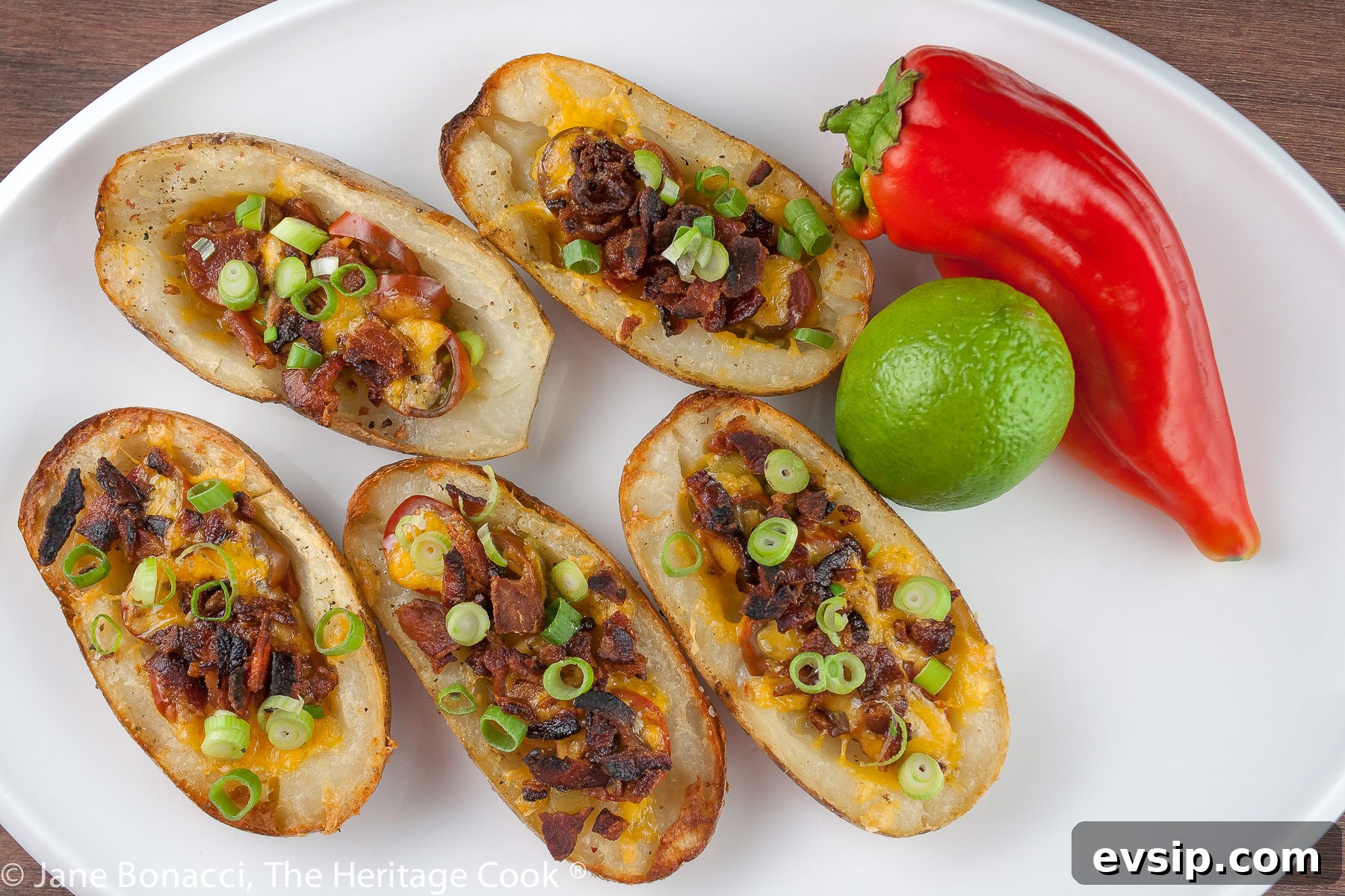 Stuffed Green Chile Potato Skins with Melted Cheese & Bacon 5 Baked potatoes are split lengthwise with the centers hollowed out and filled with crumbled bacon, green chiles, tomatoes, and melted cheese. Topped with green onions and a drizzle of taco cream. Served with lime wedges. © 2023 Jane Bonacci, The Heritage Cook.