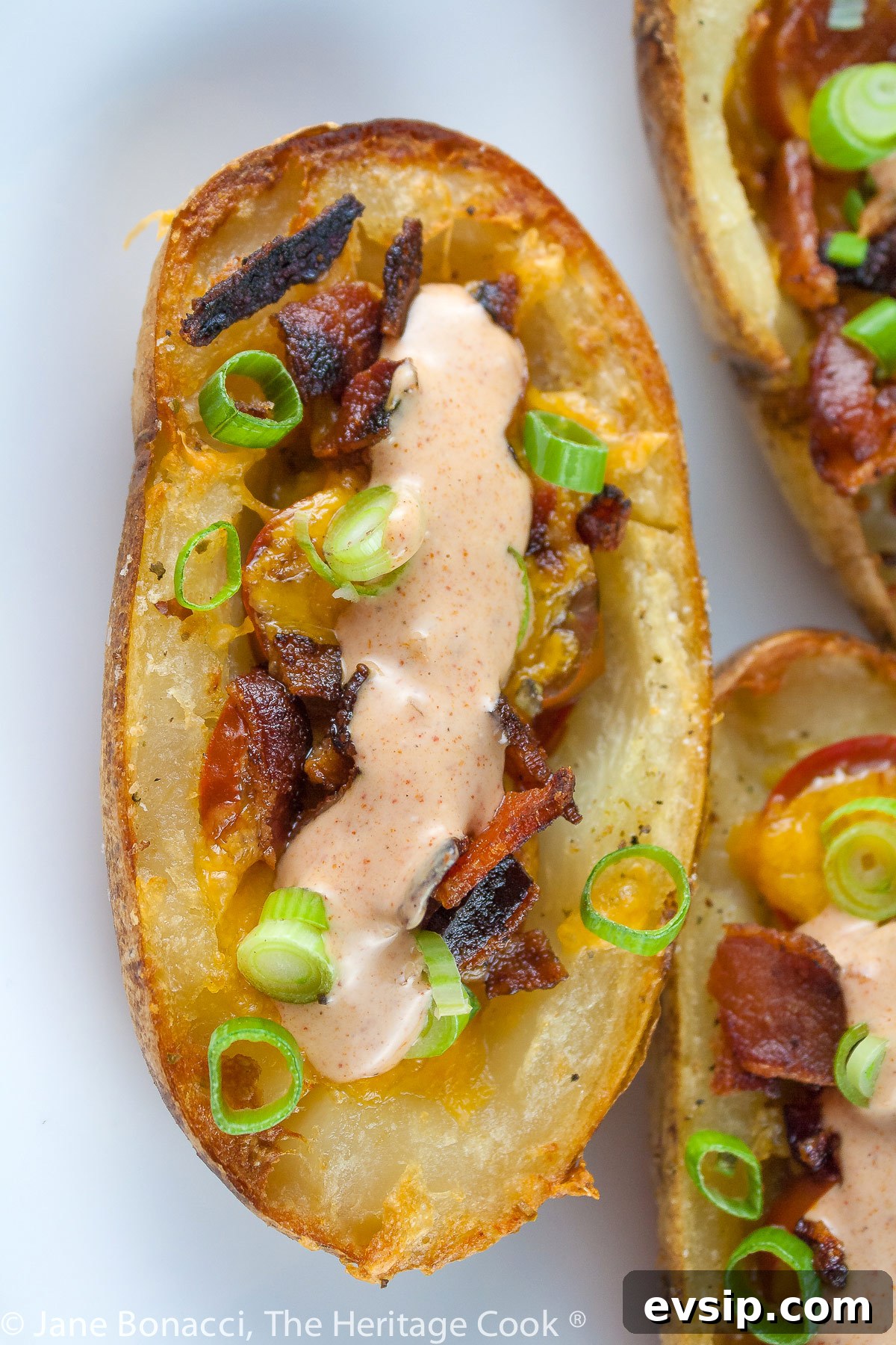 Stuffed Green Chile Potato Skins with Melted Cheese & Bacon 6 Baked potatoes are split lengthwise with the centers hollowed out and filled with crumbled bacon, green chiles, tomatoes, and melted cheese. Topped with green onions and a drizzle of taco cream. Served with lime wedges. © 2023 Jane Bonacci, The Heritage Cook.