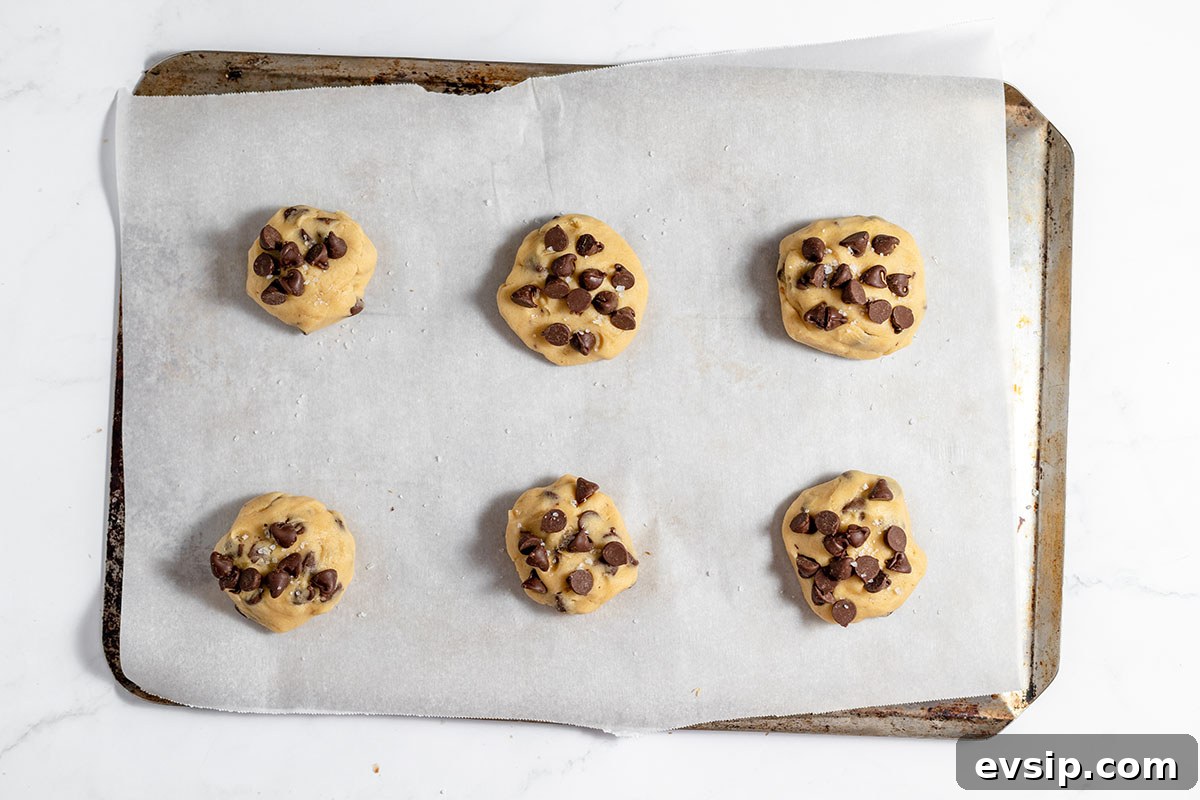 Caramel stuffed cookie dough topped with chocolate chips and sea salt on cookie sheet.
