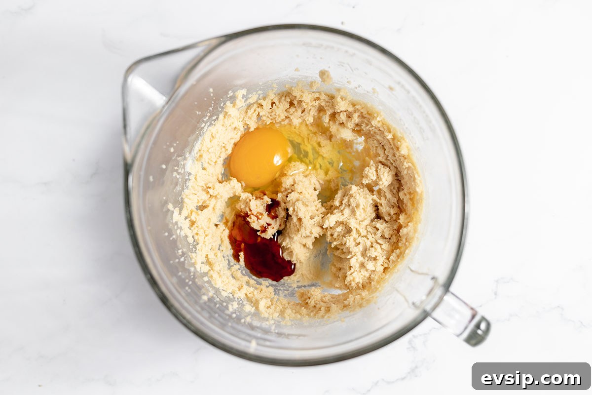Egg and vanilla extract are added to the butter-sugar mixture in a bowl.