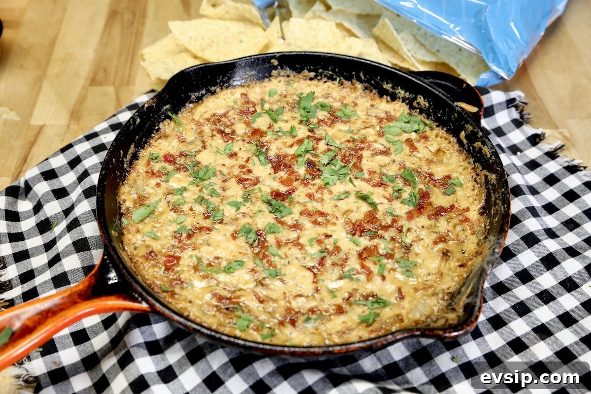 Caramelized onion dip cooked on a pellet grill. Skillet of onion dip topped with bacon, tortilla chips beside skillet.