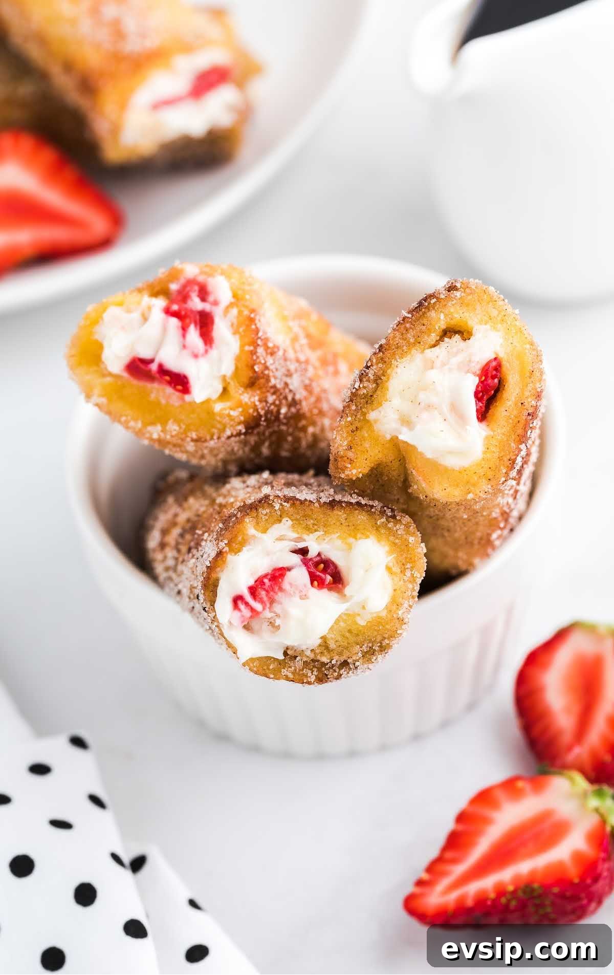 Cinnamon French Toast Roll-Ups with Maple Dipping Sauce 17 close up shot of a bowl of French Toast Roll-Ups rolled in cinnamon sugar with slices of strawberries