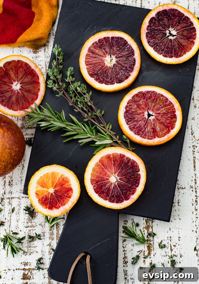 Cast Iron Seared Salmon in Blood Orange Sauce 3 Five slices of blood oranges sit on a black cutting board with sprigs of thyme and rosemary next to them. A red and orange napkin and two halves of a blood orange sit next to the cutting board.