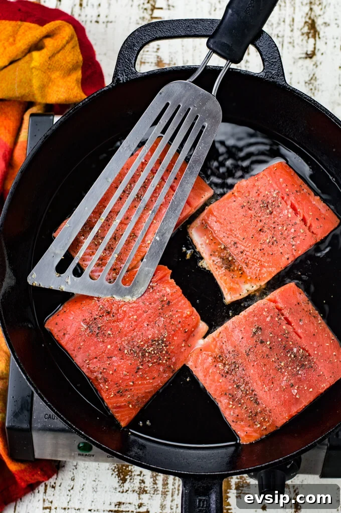 Cast Iron Seared Salmon in Blood Orange Sauce 5 Four pieces of salmon are cooking in a black cast iron skillet. A fish spatula sits on top of them. A red and orange napkin is next to the skillet.