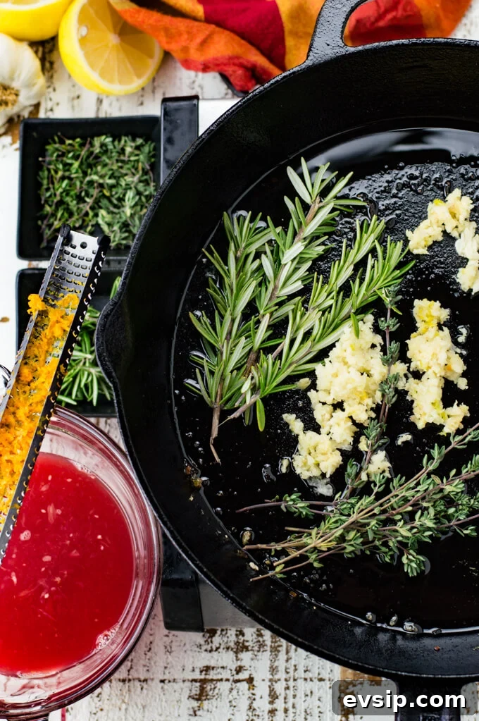 Cast Iron Seared Salmon in Blood Orange Sauce 7 Sprigs of thyme and rosemary along with minced garlic are in a black cast iron skillet. A red and orange napkin, small bowls of thyme and rosemary, a bowl of blood orange juice sit next to the skillet. A zester with blood orange zest rests on top of the bowl.