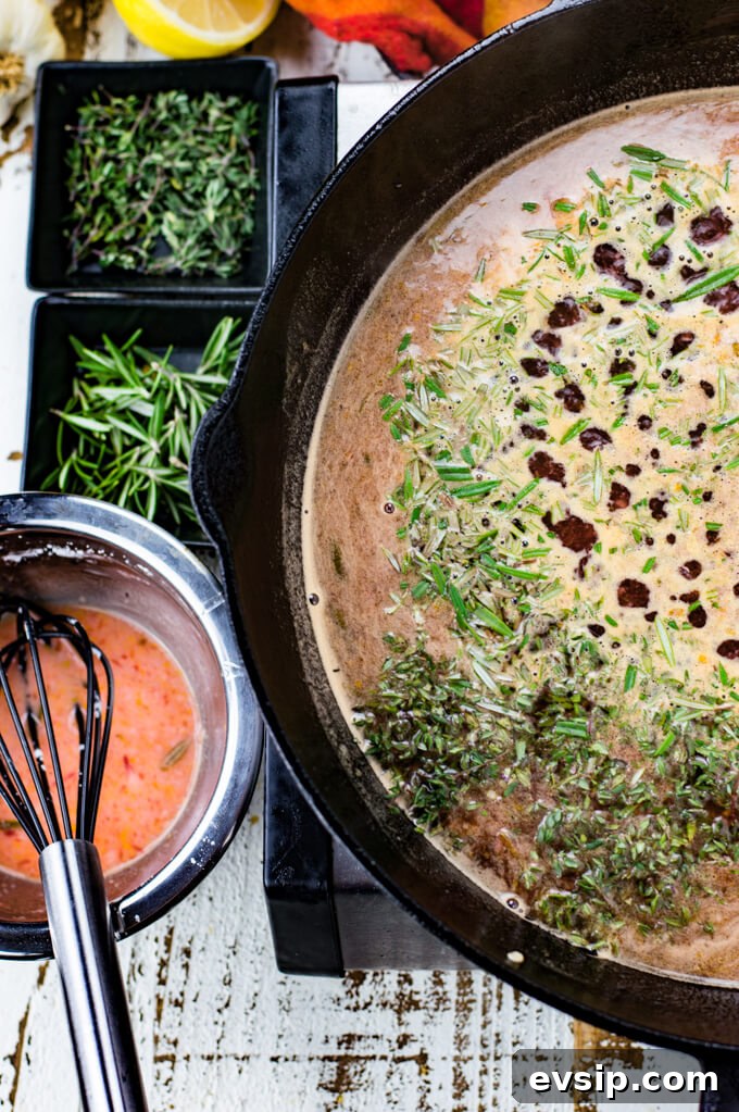 Cast Iron Seared Salmon in Blood Orange Sauce 9 Liquid for blood orange sauce boils slowly in a black cast iron skillet. Chopped thyme and rosemary are sprinkled on top. A red and orange napkin, lemon halves, more herbs and a corn starch mixture sits next to the skillet.