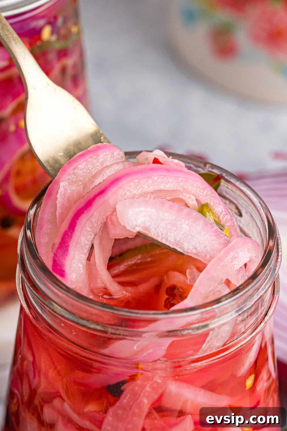 A fork pulling quick pickled red onions from a jar