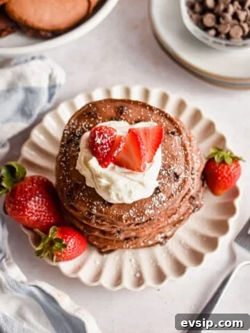An overhead shot of a stack of chocolate pancakes with pancake mix topped with strawberries and whipped cream.